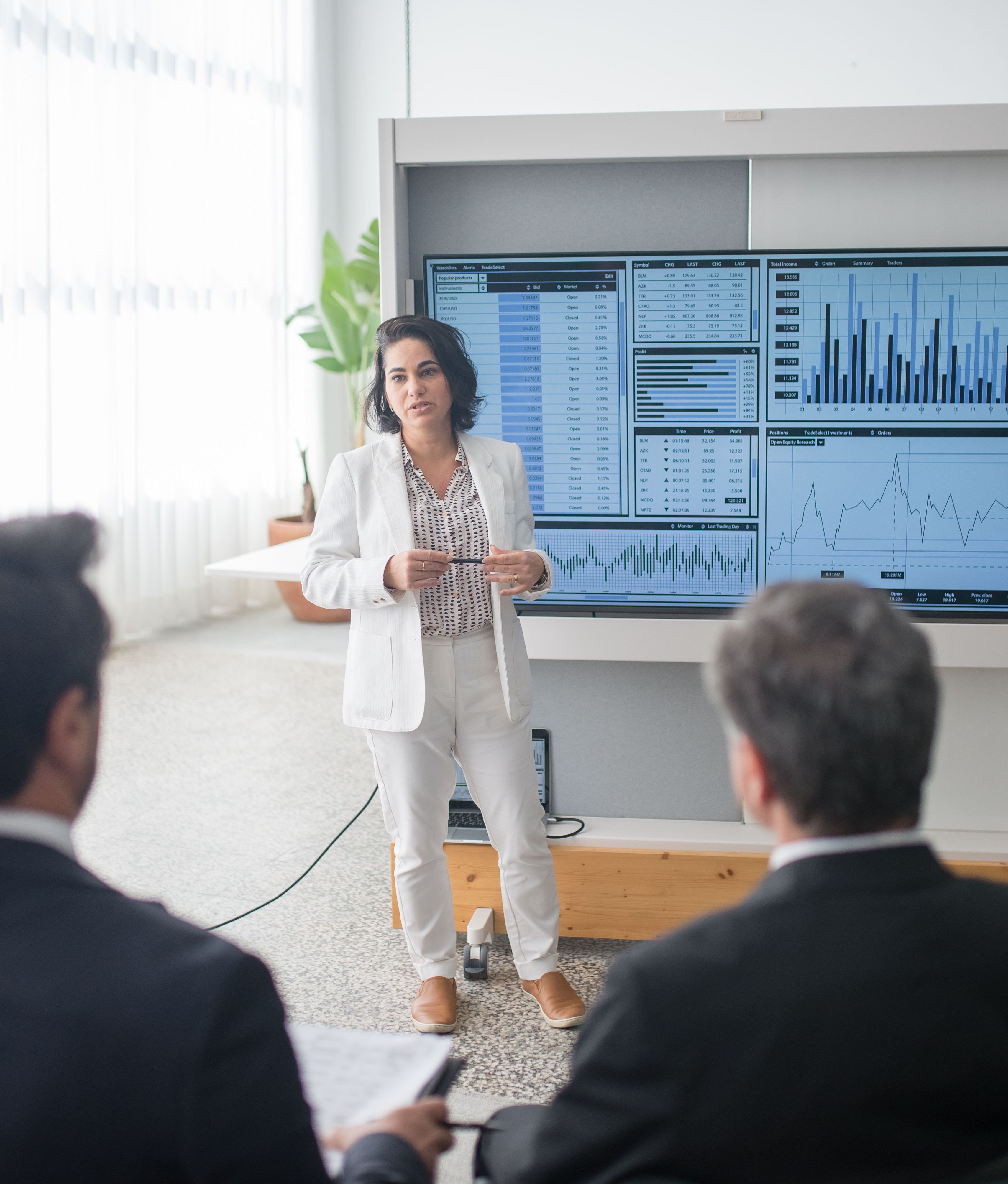 Profesional de negocios liderando una presentación ejecutiva frente a pantallas con gráficos analíticos y métricas de rendimiento.
