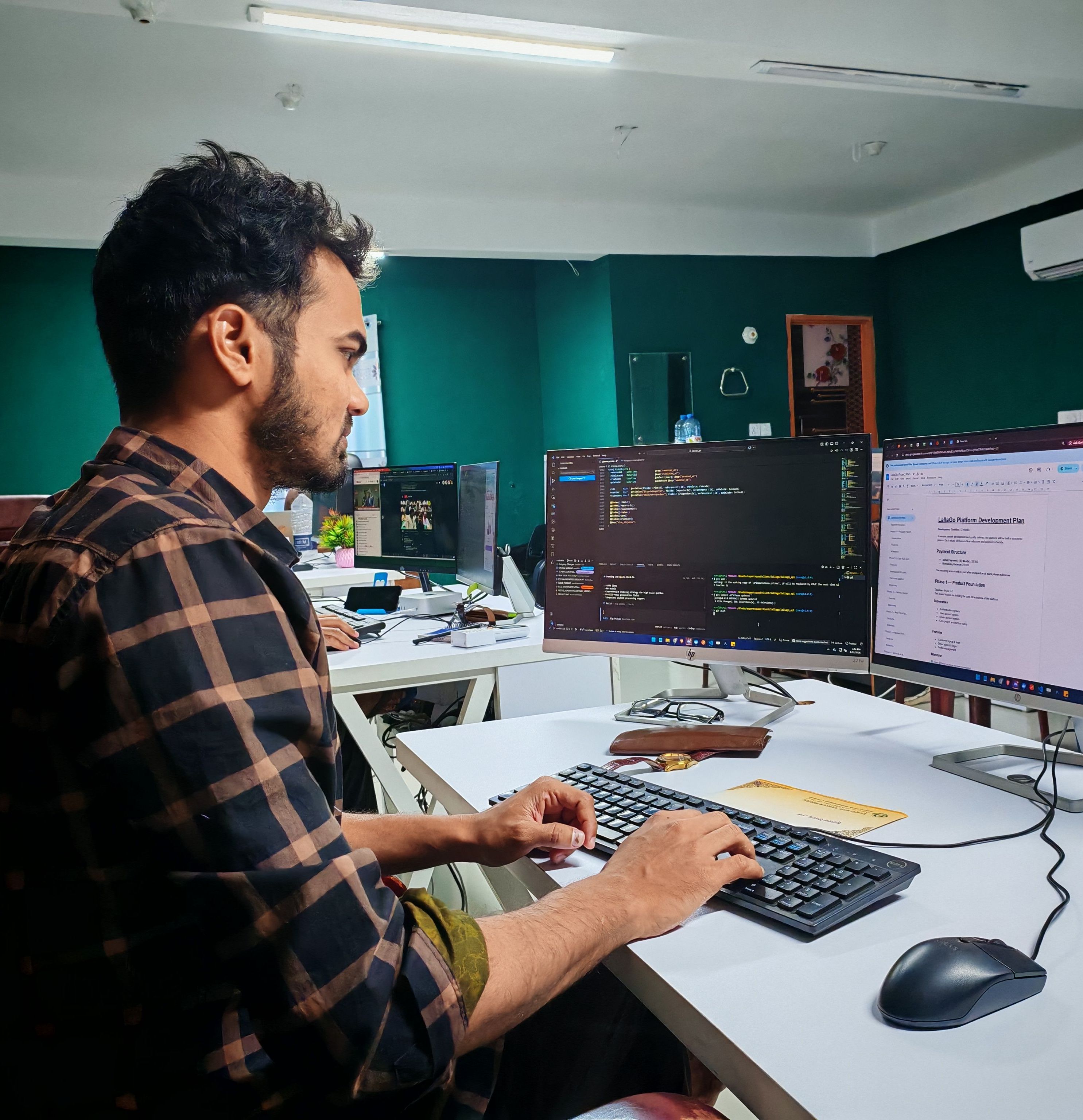 Emprendedor trabajando frente a dos monitores con líneas de código y documentación.